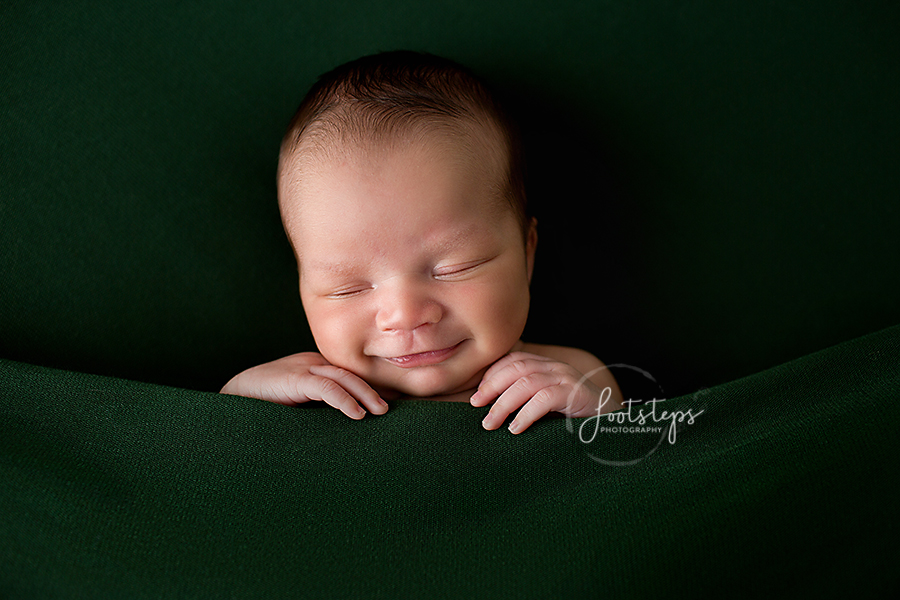 newborn snuggled up in green blankets